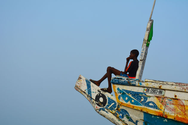 Een jongen tuurt vanaf een vissersboot naar de werkende mannen